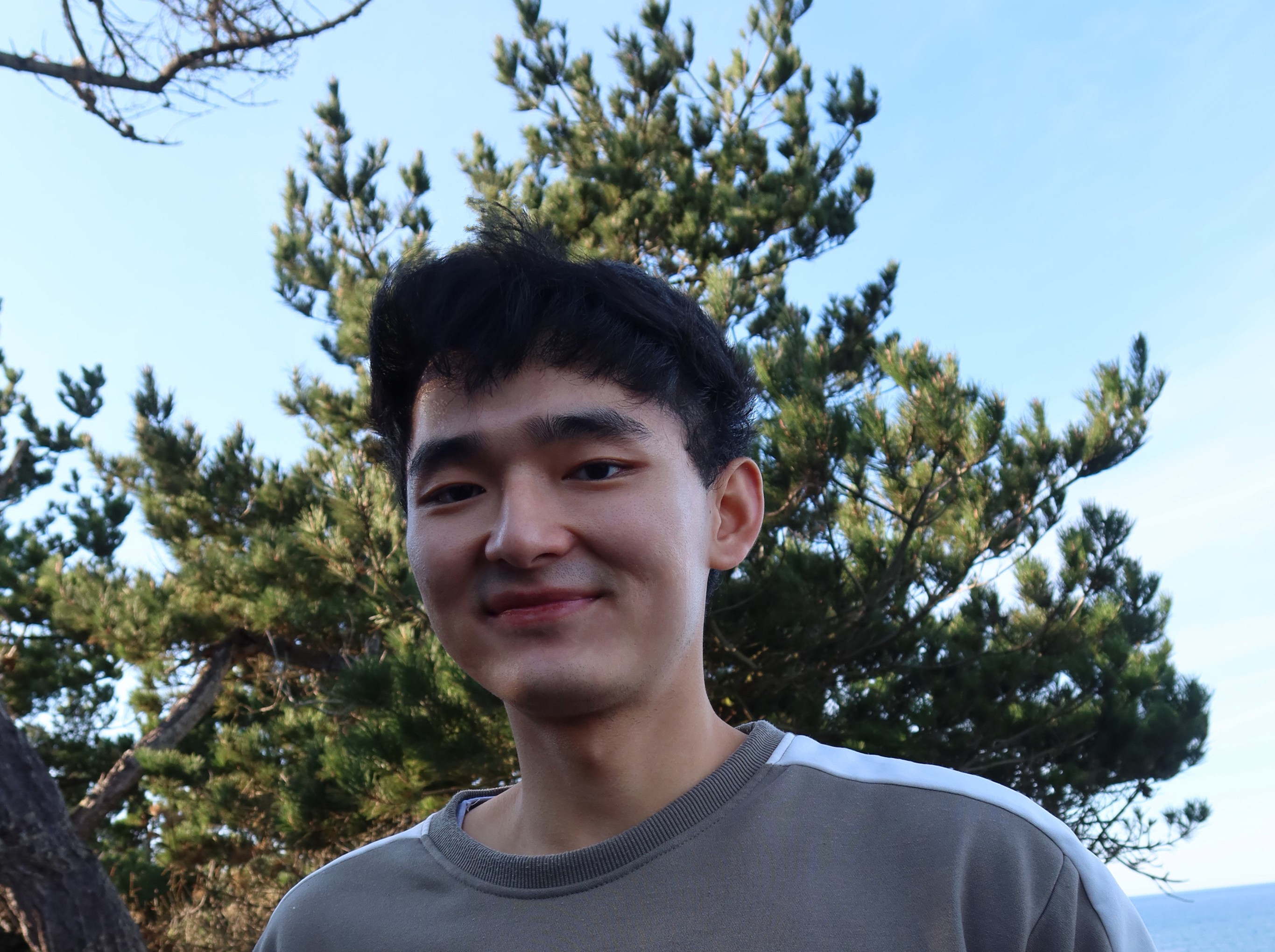 Outdoor portrait of Haoyu 'Leon' Tang, smiling, trees and water in the background.